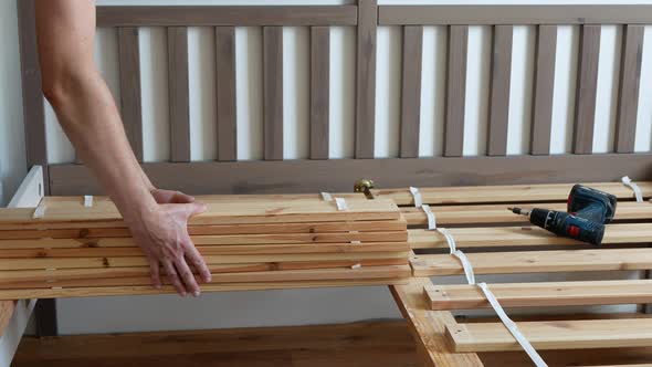 Man is setting wooden bed slats on a base to provide additional support for a mattress