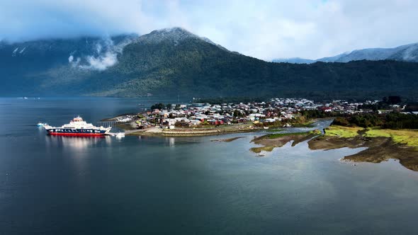 Aerial orbit of the coastline with a ferry in Hornopiren, Chile. Mountains with clouds in the backgr