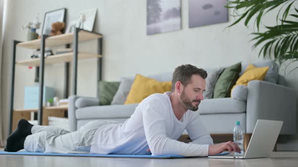 Man Using Laptop While Laying on Yoga Mat at Home