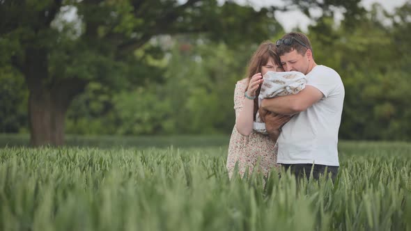 A Young Couple Standing in a Field Kissing and Holding Their Newborn Baby in Their Arms