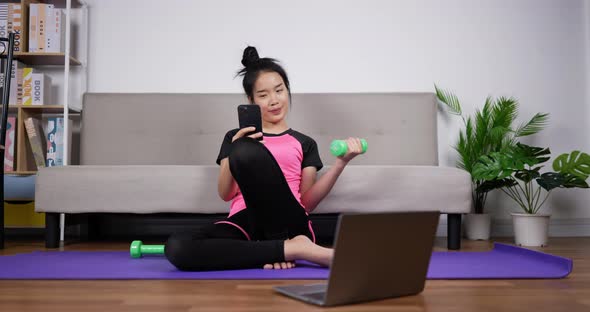 Woman holding smartphone and training dumbbells