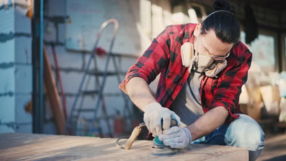 A Young Man in a Construction Respirator Grinds a Parquet Board with a Sander