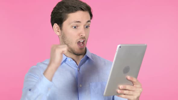 Young Man Celebrating Success on Tablet Pink Background