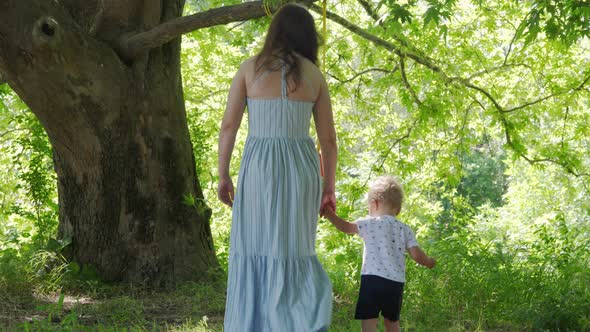 Mother with Happy Little Child Having Fun Swinging on Outdoor Baby Swing Hanging on Tree on a Sunny