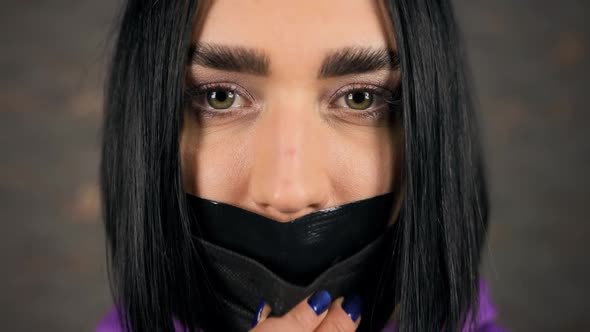 Serious Crying Young Woman Removes Black Masj Revealing Her Mouth Covered in Duct Tape