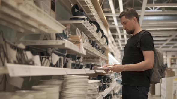Man is Inspecting Ceramic Plates in Crockery Shop Taking and Putting Back