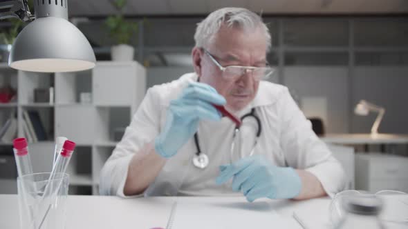 An Old Doctor in the Medical Office Holds a Test Tube with a Blood Test of a Patient with a