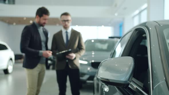 Business Man Talking To Sales Manager Choosing Car in Contemporary Showroom. Focus on Vehicle Mirror