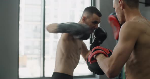 Fighter in Boxer Gloves is Practising His Strikes with Trainer in Slow Motion in the Gym Kickboxers