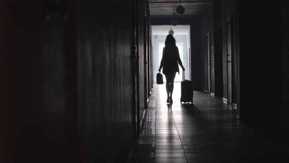 Silhouette of Female Tourist Walking with Luggage along Corridor