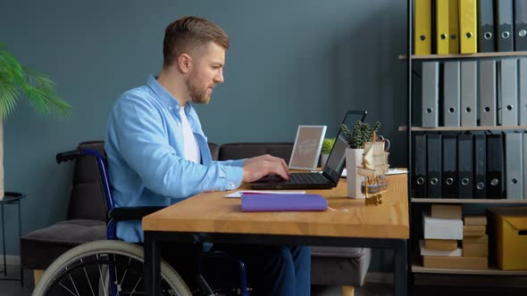 Motivated Disabled Person Freelancer is Working with Laptop Typing Sitting in Wheelchair at Office