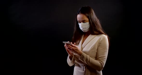 Brunette Woman with Medical Mask on Face During Coronavirus Pandemic Is Using Cell Phone