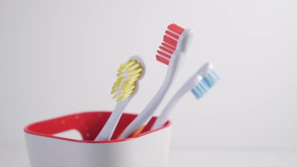 A young man pulls out a toothbrush with red bristles from a plastic glass