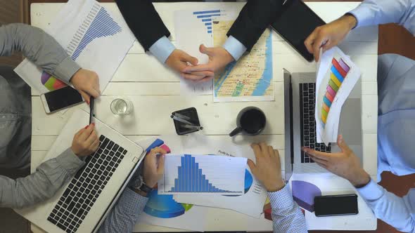 Top View to Hands of Four Business People Sitting at Table in Office and Examining Graphs