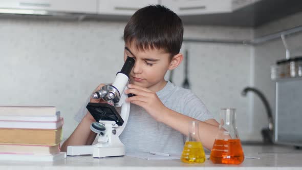 A Boy Learns Chemistry Using a Microscope and Makes Notes in a Notebook. Homework. Left Camera