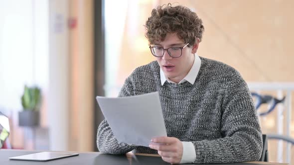 Excited Young Man Celebrating Success on Documents