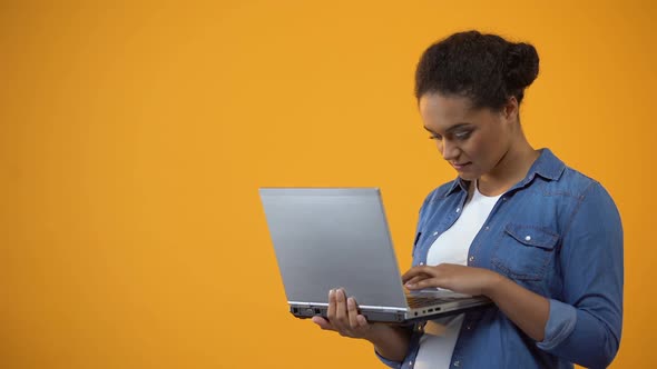 Pretty African American Woman Typing on Laptop, Isolated Yellow Background