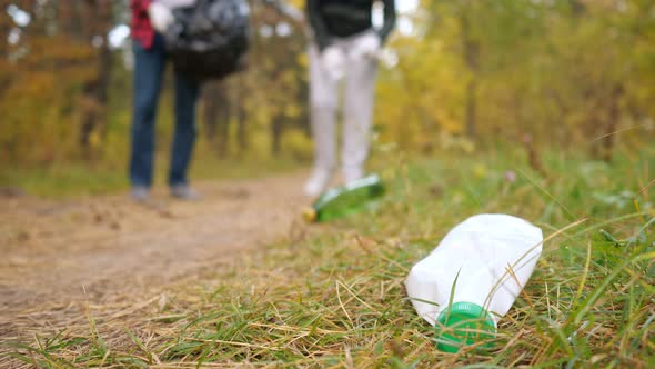 Closeup of a Plastic Bottle in the Grass Against the Background of a Couple Collecting Garbage in