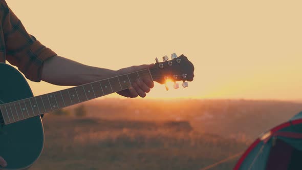 Close Man Hands with Guitar in Tourist Camp at Sunset