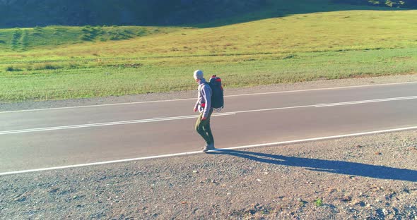 Flight Over Hitchhiker Tourist Walking on Asphalt Road. Huge Rural Valley at Summer Day. Backpack