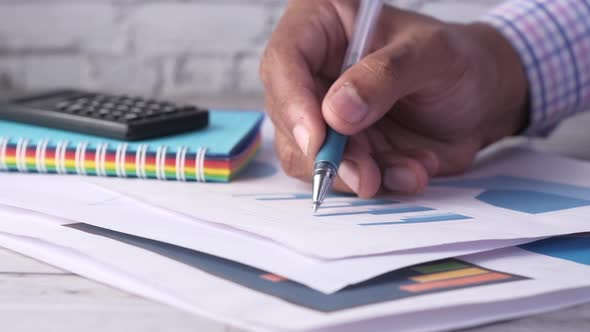 Man Hand with Pen Analyzing Bar Chart on Paper 