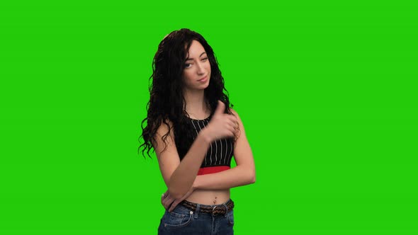 Portrait of cute brunette woman with long curly hair shows thumb up gesture on green screen