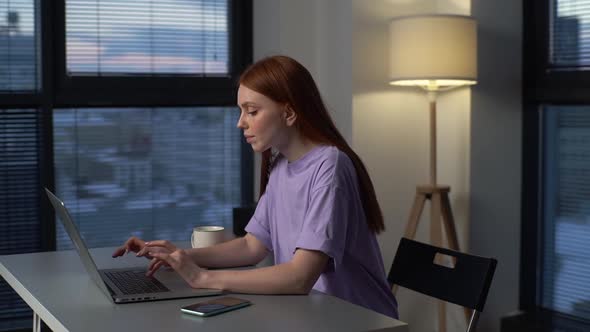 Side View of Redhead Young Woman Typing Laptop Keyboard at Evening Office Sitting at Desk Near