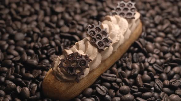 Eclair with Coffee Cream and Chocolate Pieces Lies on the Coffee Beans in the Beam of Light, Dessert