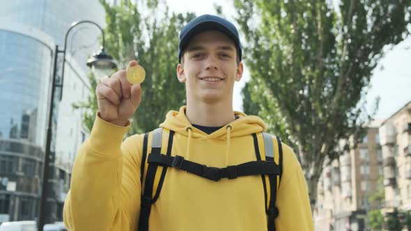 A Handsome Young Guy Shows a Golden Bitcoin in His Hand and Smiles