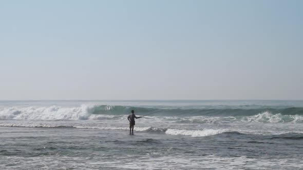 Local Fisherman Holds Rod in Hand in Waving Blue Ocean