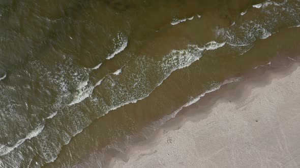 Topdown Of Foamy Waves Rolling Into Sandy Coastline Of Baltic Sea. Aerial Drone