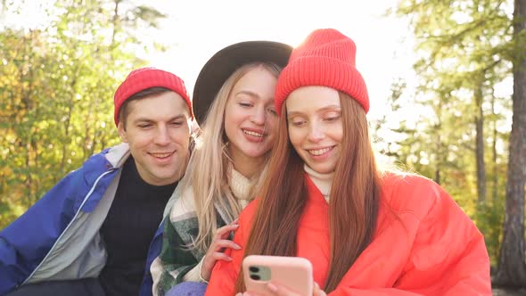 Three Caucasian Friends Look at Photos They Took in Forest