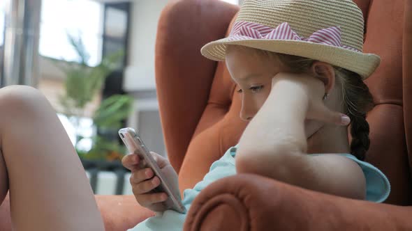 Beautiful Little Girl Use of Mobile Phone Sitting in the Lobby of the Hotel.