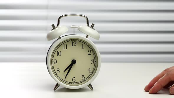 round white alarm clock rings on the table, hand tries to find and stop