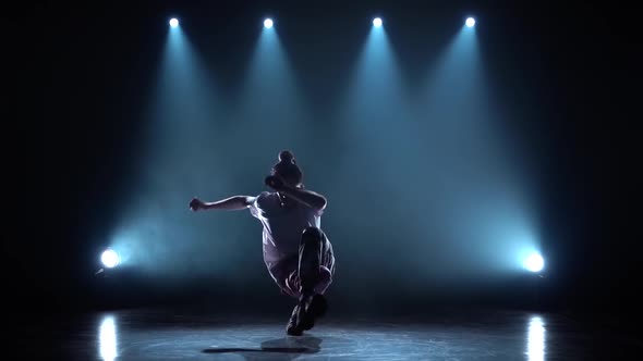 A Young Guy Performs Modern Hip Hop Dance on the Dark Studio with Smoke and Lighting, Twisting and