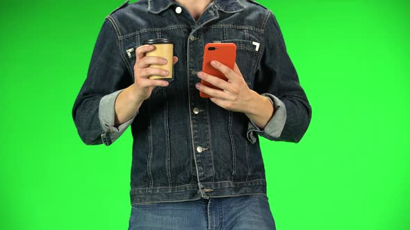 Guy Holding Red Phone in Her Hands and Drinking Coffee While Walking, Close Up. Green Screen