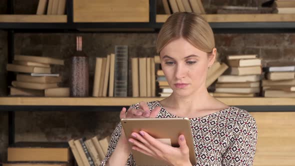 Good Looking Woman Using A Tablet near bookshelf. Beautiful girl touch computer pad screen at home 