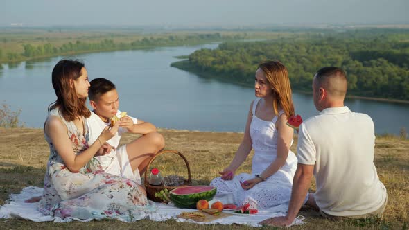 Girl and Boy Eat Sandwiches with Parents at Festive Picnic