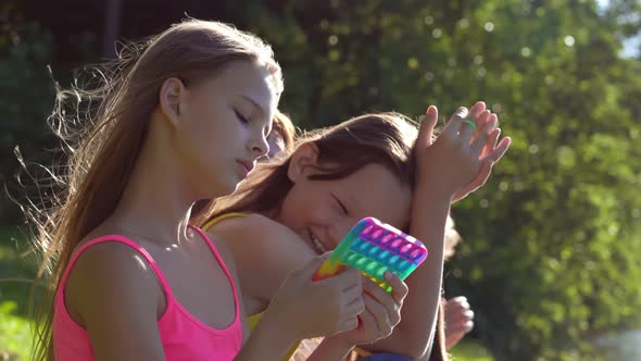 Portrait of Teen Girl Playing with Trendy Pop It Toy with Friends Sitting on Background