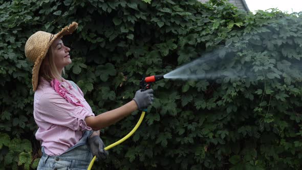 A Young Adult Woman Wateres a Vegetable Garden with a Garden Hose Outside the House