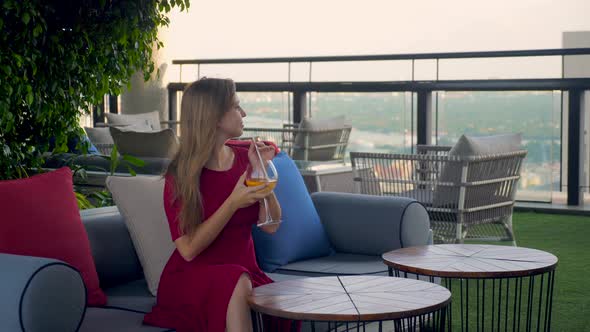 Beautiful Young Woman with Cocktail Drink at Luxury Rooftop Restaurant Enjoy Cityscape During Sunset