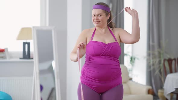 Confident Obese Woman Posing with Measuring Tape Indoors at Home Looking at Camera Smiling