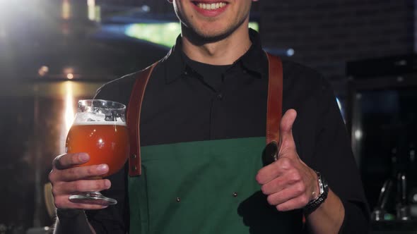 Unrecognizable Brewer in Apron Showing Thumbs Up, Holding Glass of Beer