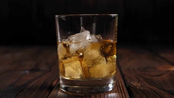 A Glass of Whiskey with Ice on a Wooden Background in the Dark