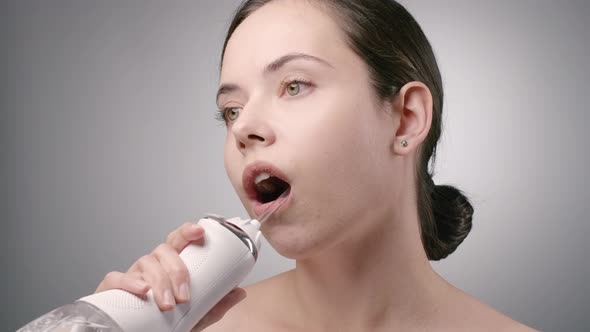 Young Brunette Woman Cleaning Teeth with Water Flosser in Bathroom