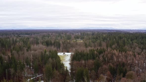 Drone flight backwards away from a idyllic placed house in the middle of a wide forest at the winter