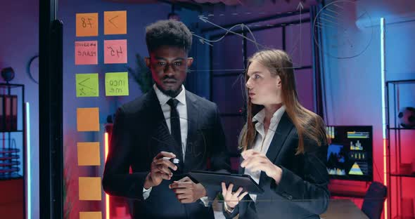 Businessman with Pretty Concentrated European Female Colleague Working Together Near Glass Wall