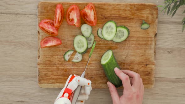 Man with Robotic Prosthetics Hand with Knife on It Is Trying To Cut Cucumber for Slices on Wooden