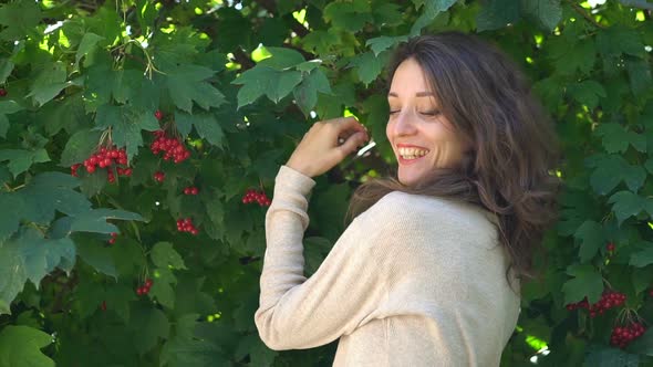 Front View of Young Woman on Big Green Tree with Red Berries Background Posing to Camera with Smile