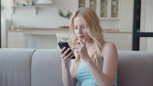 Millennial Woman Sit on Sofa Holding Smartphone Read Great News on Sms Feels Overjoyed Clenched Fist